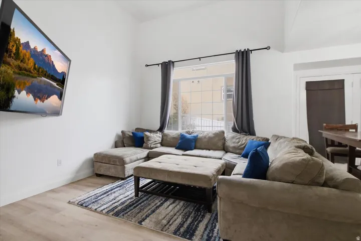 Vaulted ceilings enhance this living space featuring light wood-finish flooring and a large window with privacy blinds