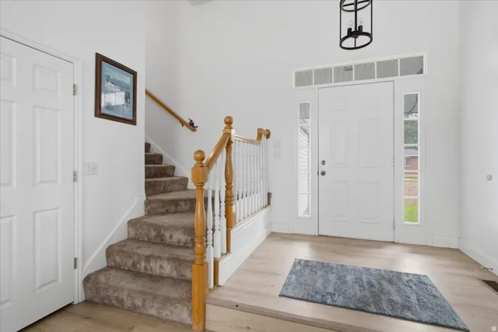 Entryway featuring a double panel front door with transom and sidelight windows, light wood-finish flooring, and a carpeted staircase with wood banister