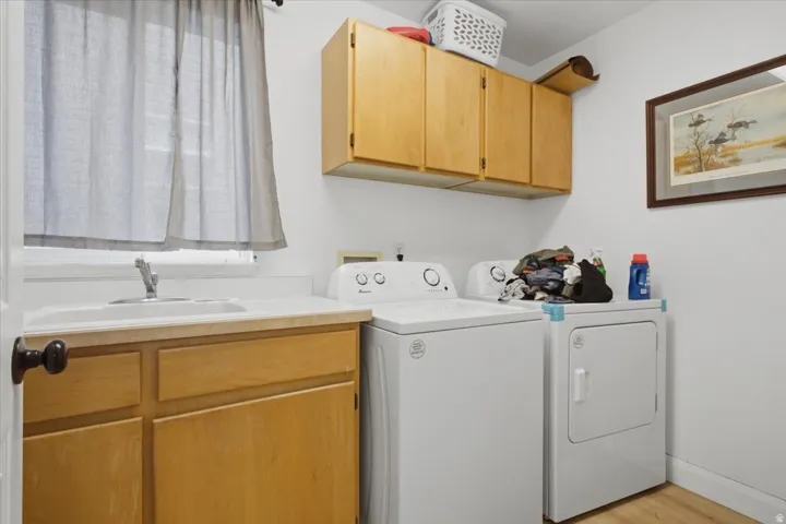 Dedicated laundry space featuring a utility sink, light wood-finish cabinetry, and overhead storage