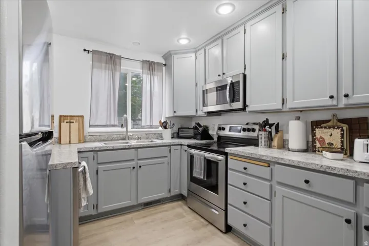 Contemporary kitchen featuring light gray cabinetry, speckled countertops, stainless steel appliances, and recessed lighting