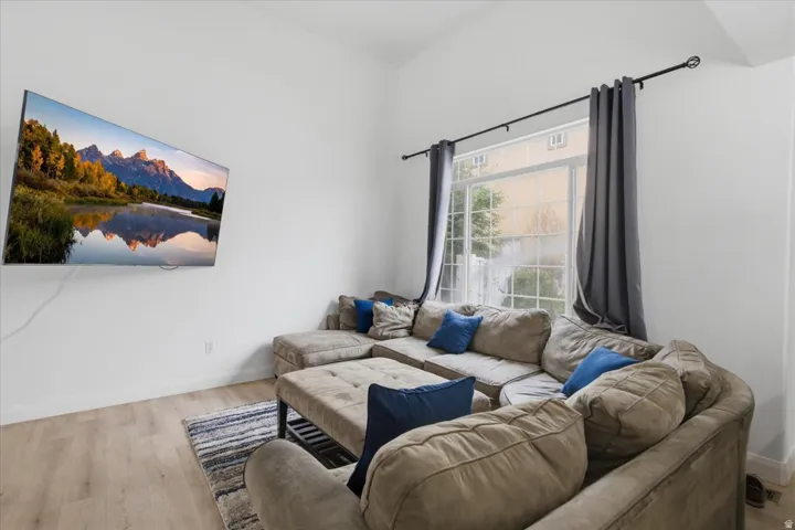 Living area with vaulted ceilings, light wood-finish flooring, and a large window providing natural light