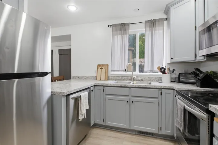 Kitchen featuring light gray cabinetry, stainless steel appliances, speckled countertops, and a window above the sink