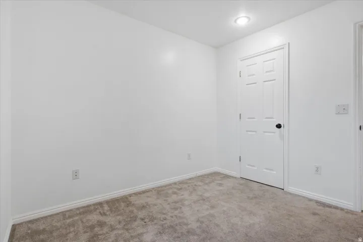 Carpeted room featuring white walls, a six-panel door with a black doorknob, and recessed ceiling lighting