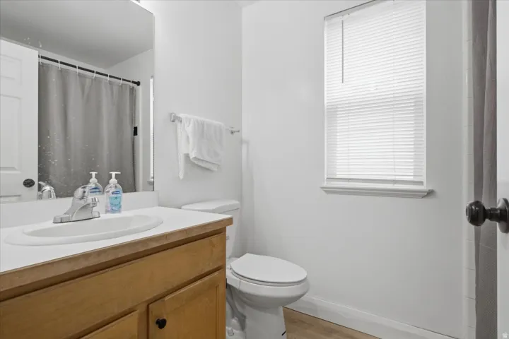 Bathroom featuring a wood-finish vanity with a white countertop, an oval undermount sink, a chrome faucet, and a toilet