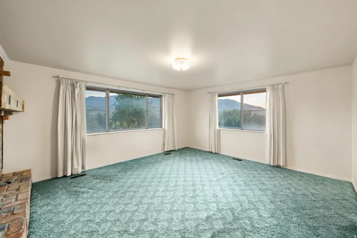 Spacious interior featuring a brick fireplace, two large windows with mountain scenery, wall-to-wall carpeting, and a flush-mount ceiling light fixture