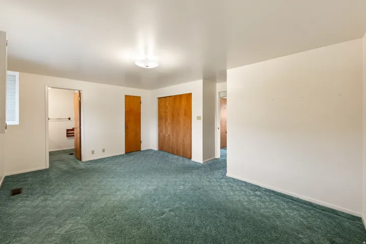 Expansive carpeted room featuring a ceiling-mounted light fixture, white walls, and a window with blinds
