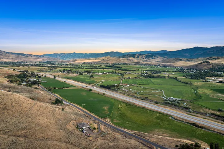 Expansive aerial landscape featuring a highway, green fields, and distant mountains