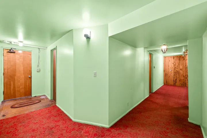 Hallway featuring red patterned carpet, light green painted walls, and overhead lighting fixtures
