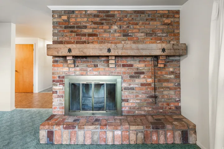 Brick fireplace featuring a wood mantel, brass firebox enclosure, and hearth