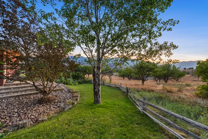 Expansive outdoor space featuring a split rail fence, mature trees, and natural landscaping with distant mountains