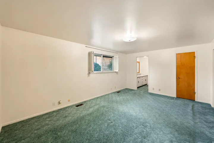 Spacious room featuring light-colored walls, green carpeting, a window with exterior shutters, and a flush-mount ceiling light fixture