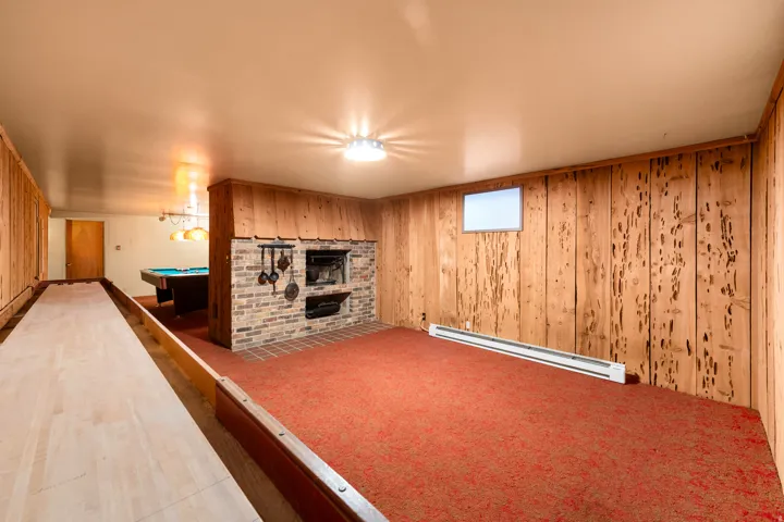 Spacious recreation room featuring wood paneling, a brick fireplace, and red carpet