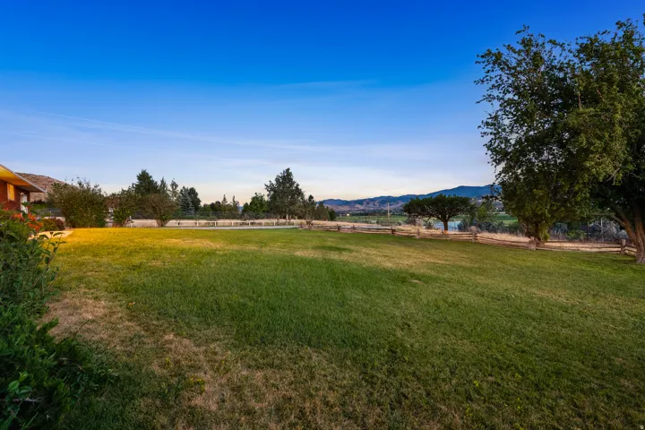 Expansive grassy lawn bordered by mature trees and a rustic split-rail fence