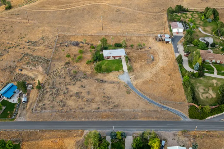 Expansive property featuring a single-story residence with a light-colored roof, a gravel driveway, and surrounding arid landscaping