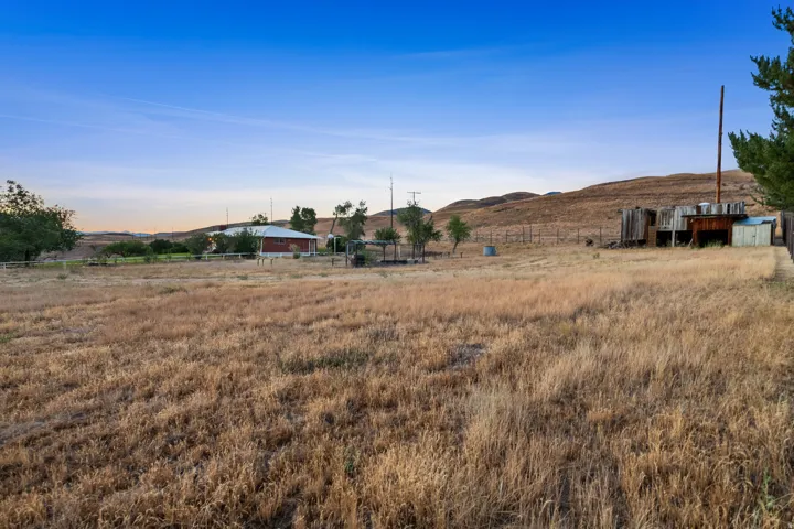 Expansive rural property featuring a red single-story structure and distant rolling hills