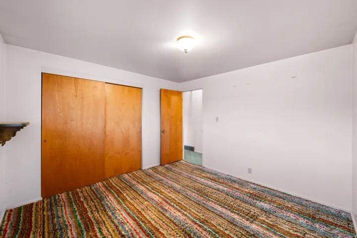 Room featuring a colorful striped rug, light wood-finish sliding closet doors, and white painted walls
