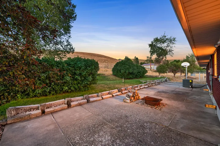 Expansive concrete patio featuring a built-in fire pit, stone planter beds, and a basketball hoop