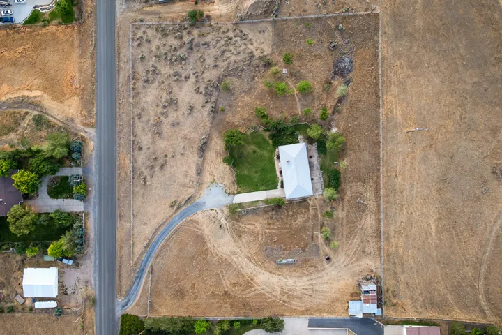 Overhead property view featuring a residence with a light-colored roof, a verdant lawn area, and a gravel driveway