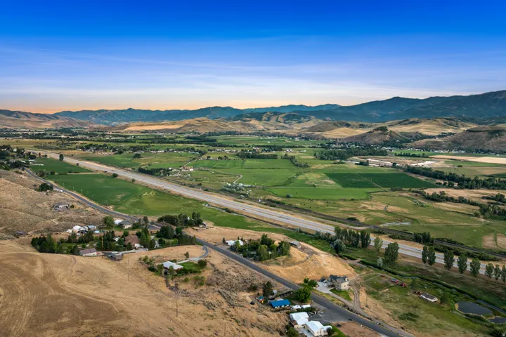 Expansive rural landscape featuring a highway, green fields, and distant mountains under a blue sky
