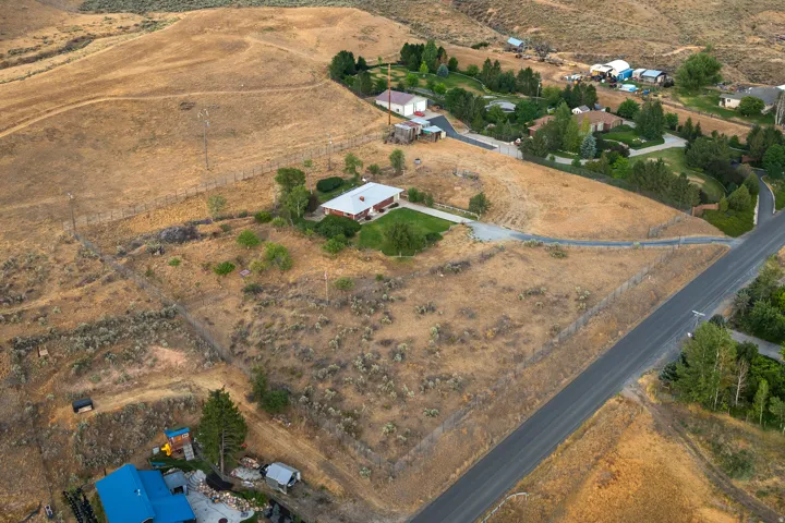 Expansive rural property featuring a single-story residence with a red roof, a gravel driveway, and a partially fenced perimeter