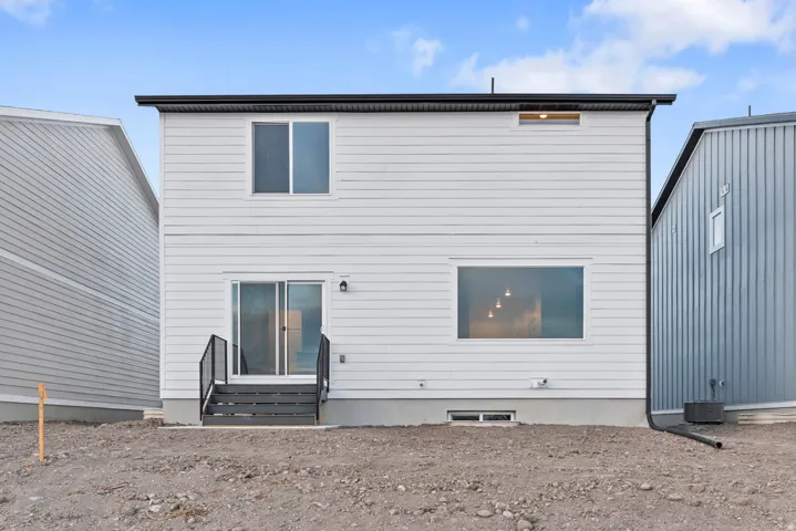 Rear exterior featuring white horizontal siding and a sliding glass door leading to dark-toned outdoor steps with black railings