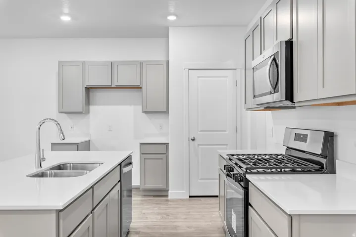 Modern kitchen featuring light gray cabinetry, white countertops, stainless steel appliances, and wood-finish flooring