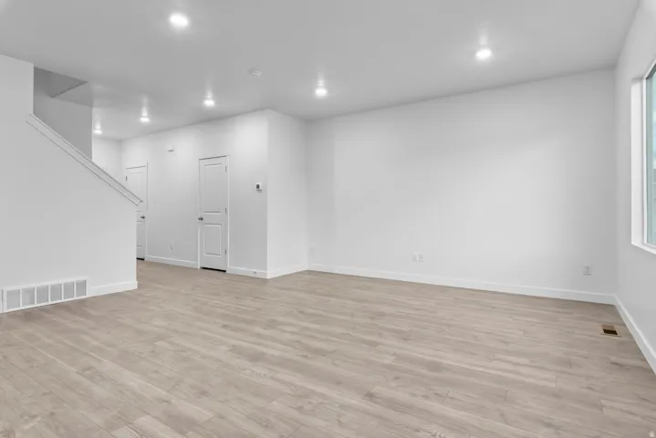Open-concept living space featuring wood-finish flooring, recessed lighting, white walls, and a prominent window