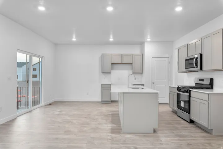 Open-concept kitchen and living area featuring wood-finish flooring, recessed lighting, and a sliding glass door to an outdoor patio