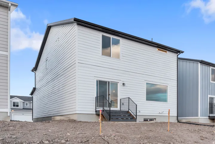 Rear exterior featuring light-toned siding, a black roofline, and a sliding glass door with a deck and black railing