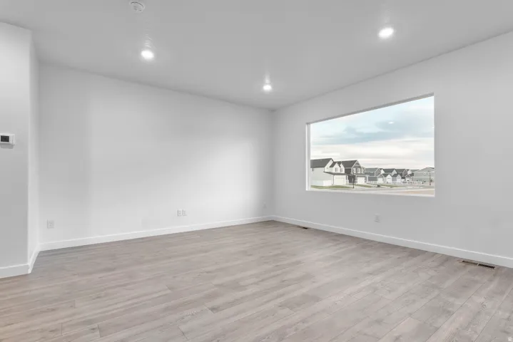 Bright interior space with light-tone wood-finish flooring, recessed ceiling lighting, and a horizontal picture window