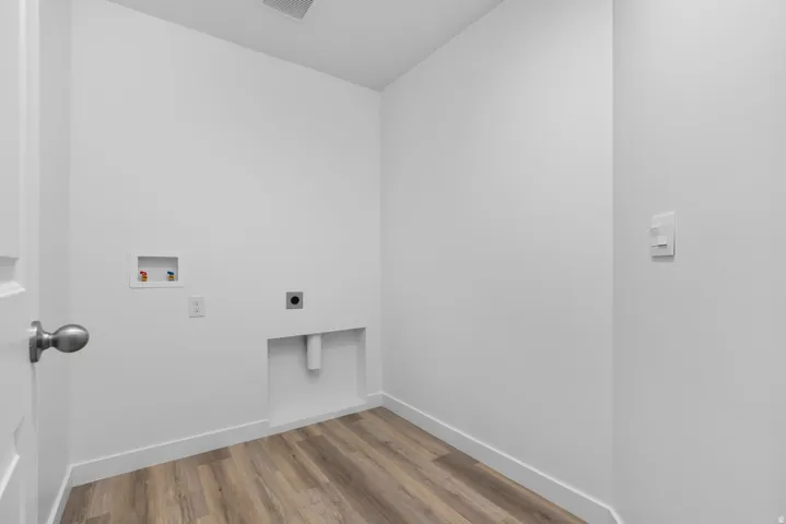 Dedicated laundry area featuring wood-finish flooring, white walls, and essential utility connections