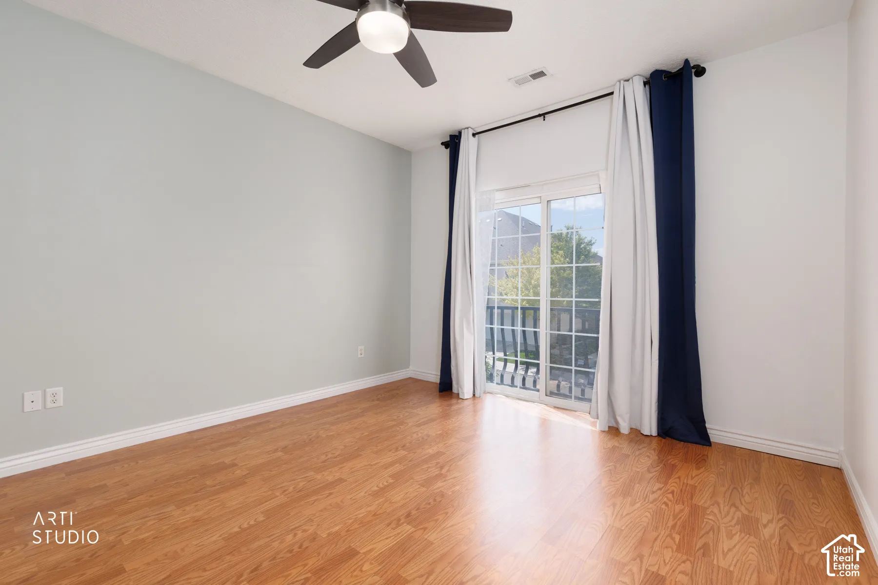 Spacious room featuring wood-finish flooring, a contemporary ceiling fan, and a sliding glass door leading to a private balcony
