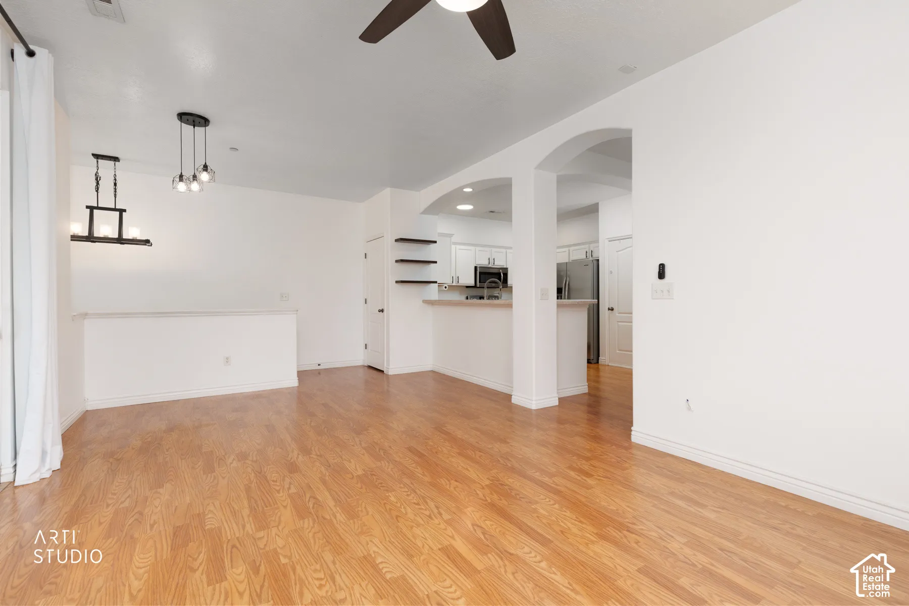 Open-concept living area featuring wood-finish flooring, a contemporary linear chandelier, an additional multi-bulb pendant light, and a built-in ceiling fan