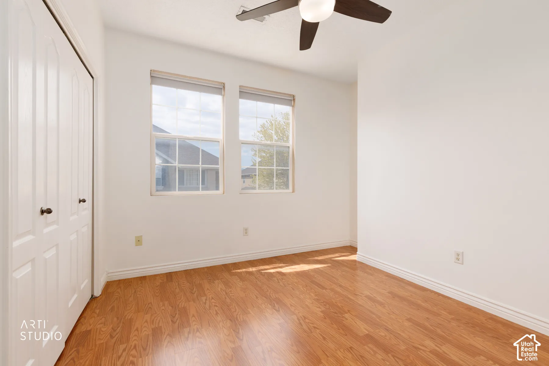 Bright interior space featuring wood-finish flooring, a ceiling fan, and dual windows with blinds