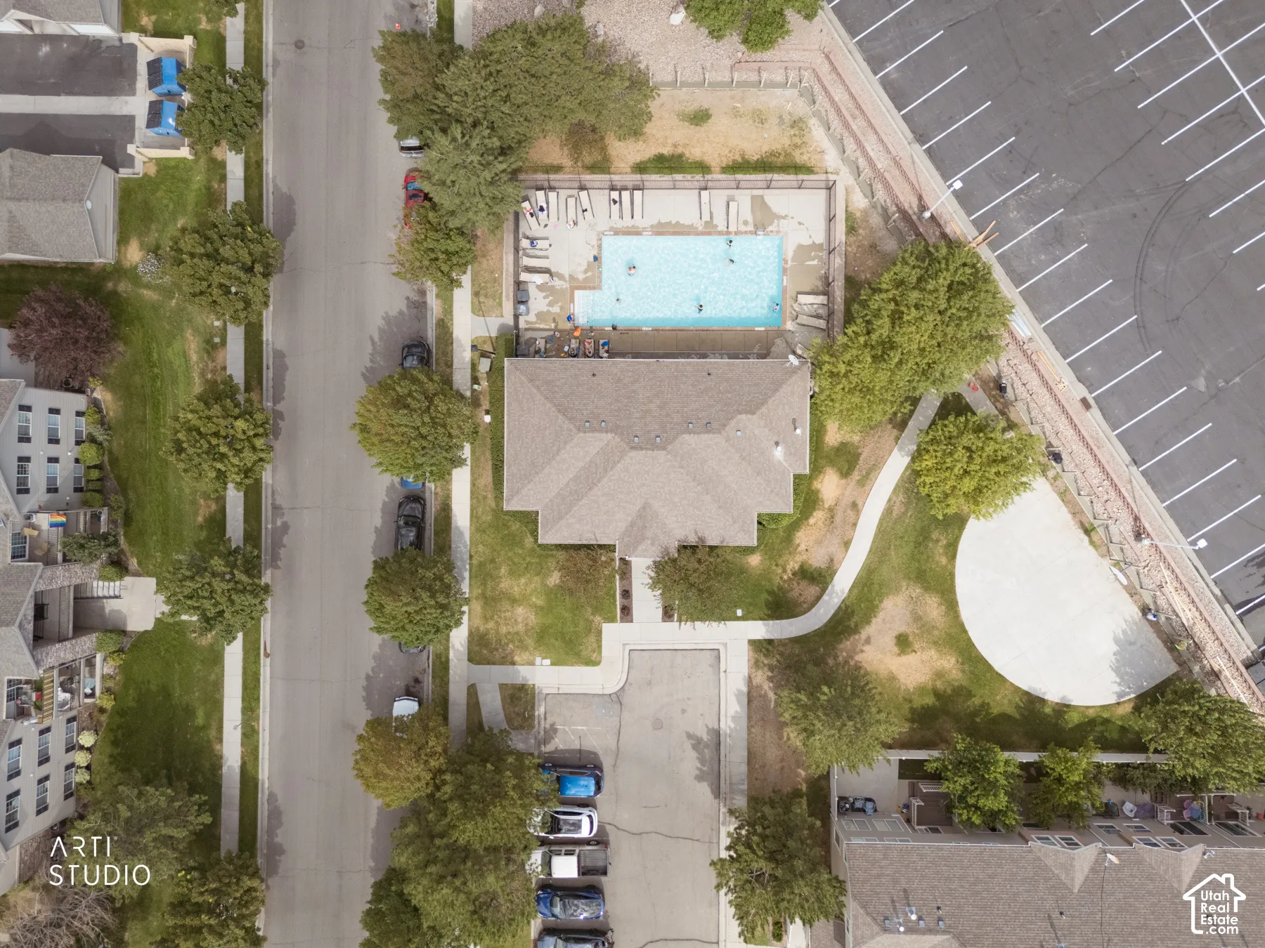 Central property with a gabled roofline, featuring a swimming pool with surrounding lounge areas, an expansive open lawn, and mature trees