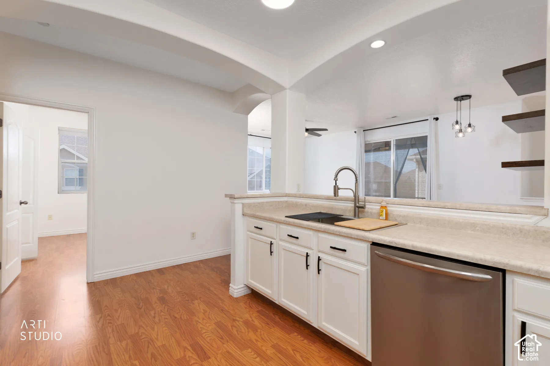 Kitchen featuring white cabinetry with black hardware, stainless steel dishwasher, light-toned countertop, and a stainless steel sink with a high-arch faucet