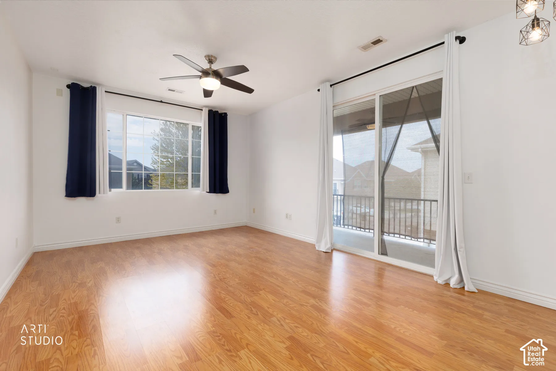 Spacious room featuring wood-finish flooring, a ceiling fan with integrated lighting, and a large window with white trim
