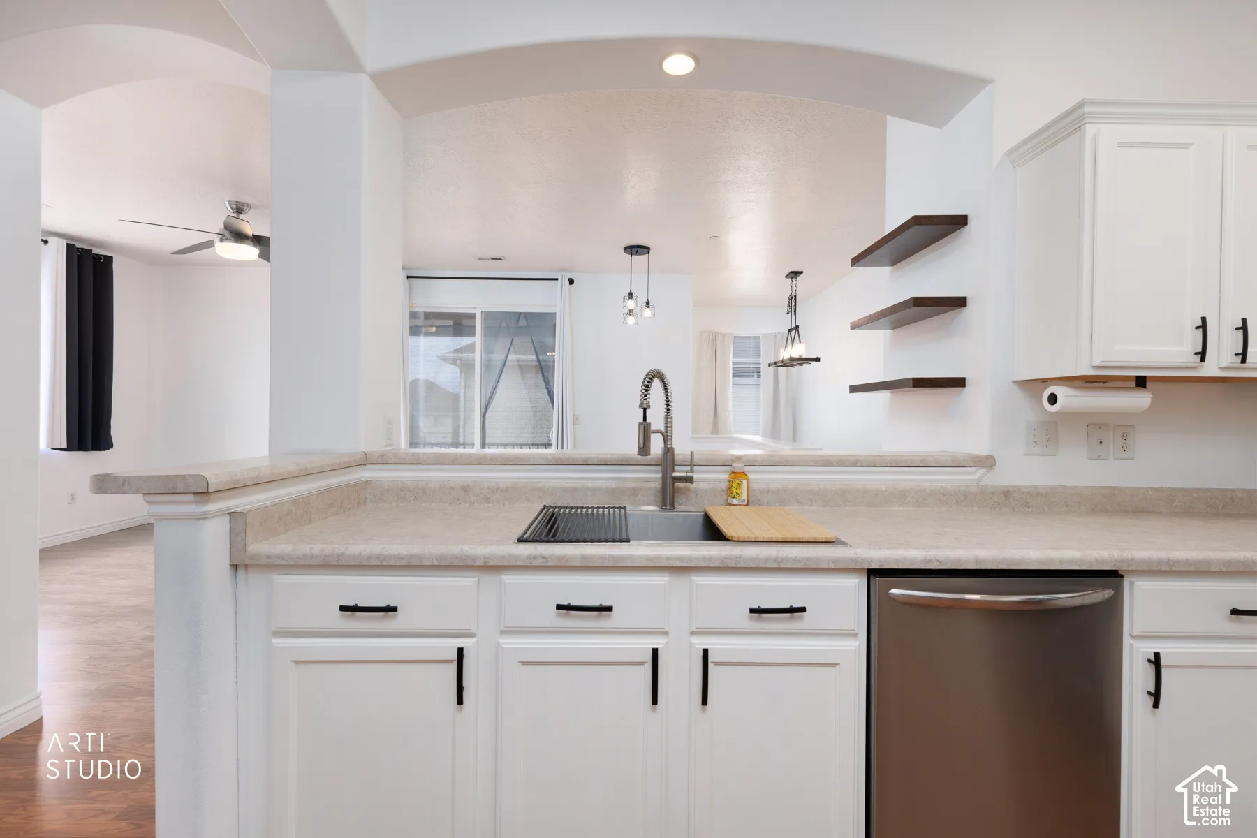 Kitchen featuring white cabinetry with black hardware, an integrated sink with a gooseneck faucet, light-toned countertops, and a stainless steel dishwasher