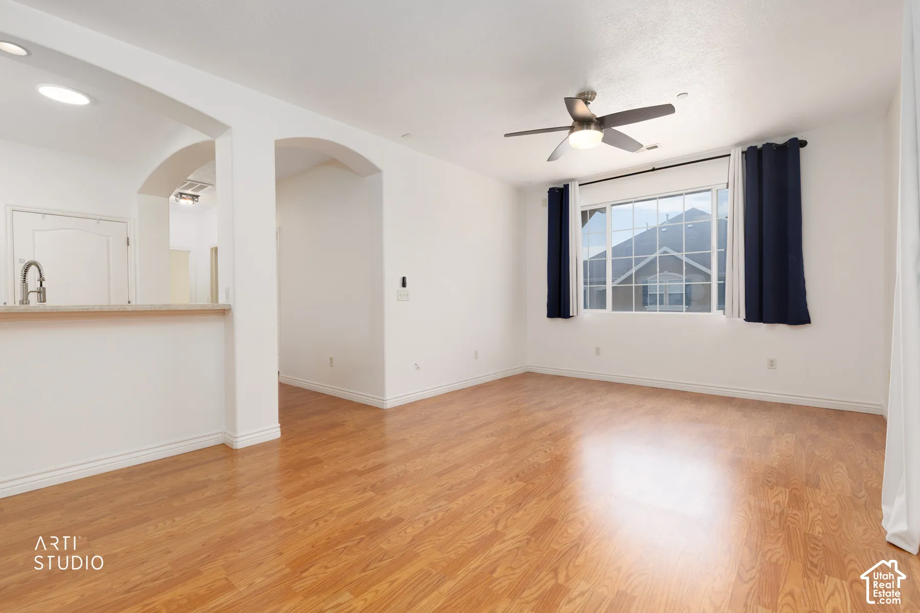 Open-concept living space featuring wood-finish flooring, a contemporary ceiling fan, and a large window with white muntins