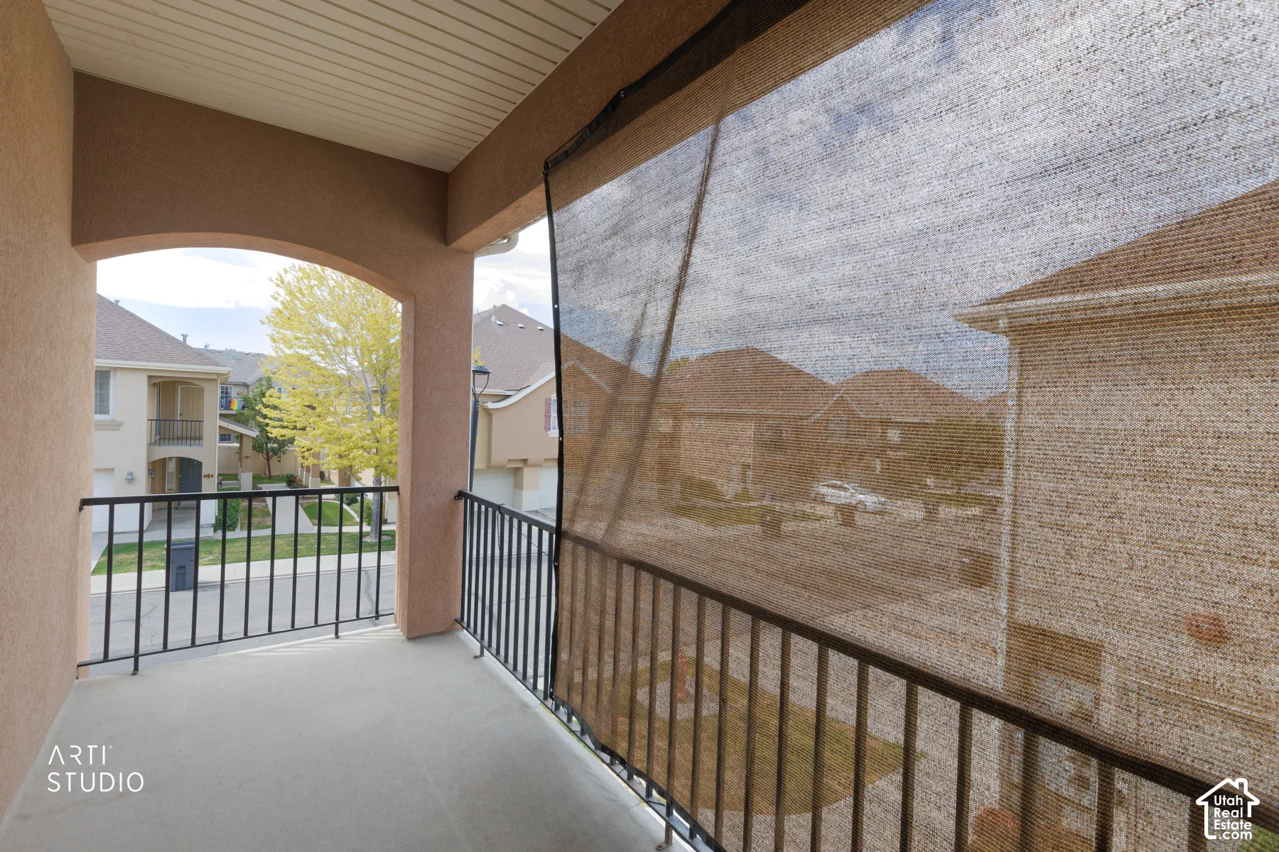 Covered outdoor balcony featuring a neutral-toned ceiling, stucco archway, durable concrete flooring, and black metal railings