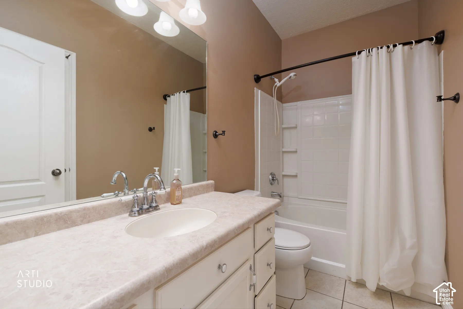 Bathroom featuring a white vanity with an integrated sink, a large wall-mounted mirror, a three-light fixture, a shower-tub combination with a white subway tile surround, and neutral floor tiling