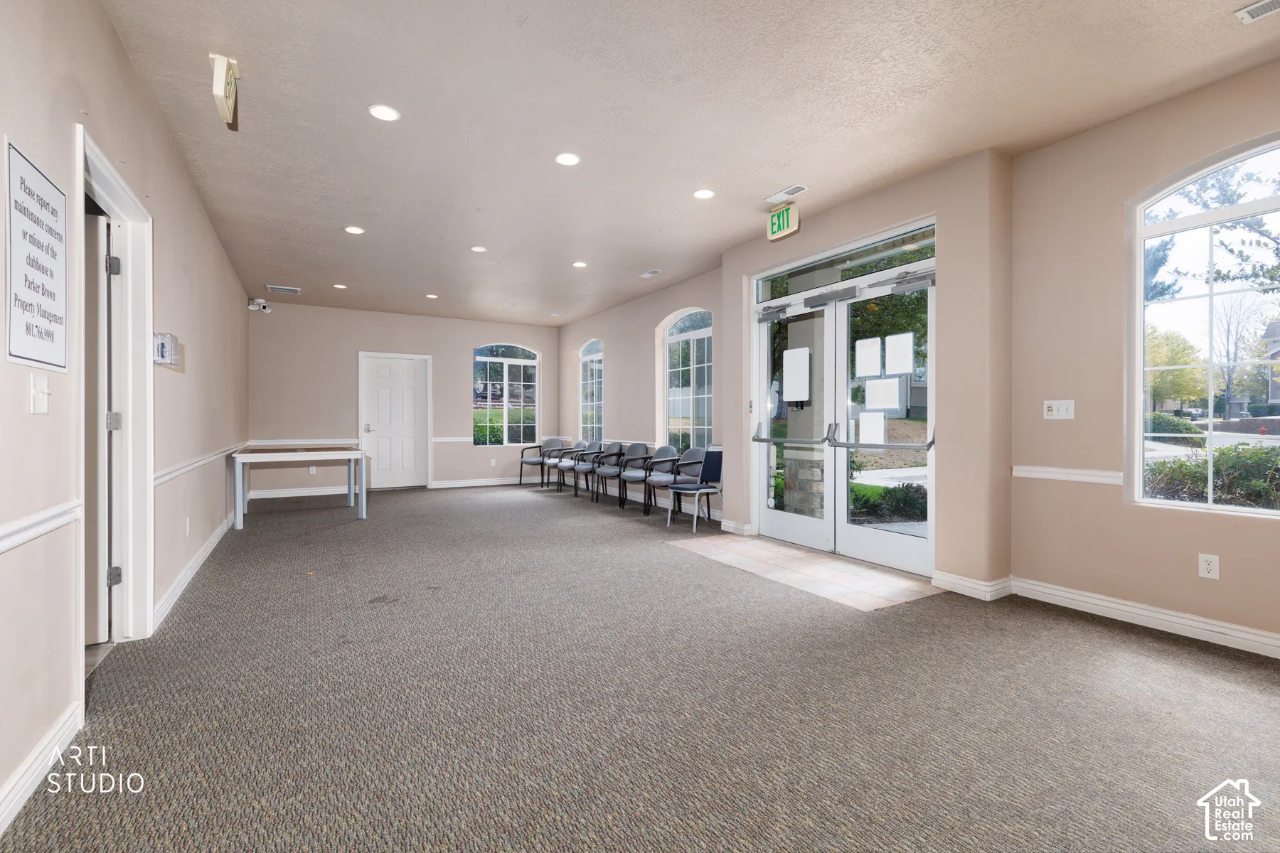 Spacious room featuring neutral carpeting, recessed lighting, arched windows with grid patterns, a glass-paneled entry door, and painted trim molding