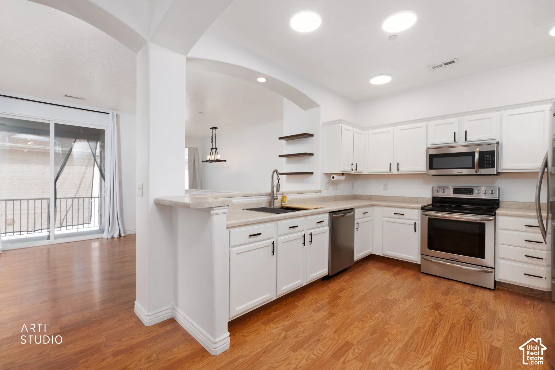 Kitchen featuring white cabinetry with dark hardware, stainless steel appliances, light-toned countertops, and wood-finish flooring