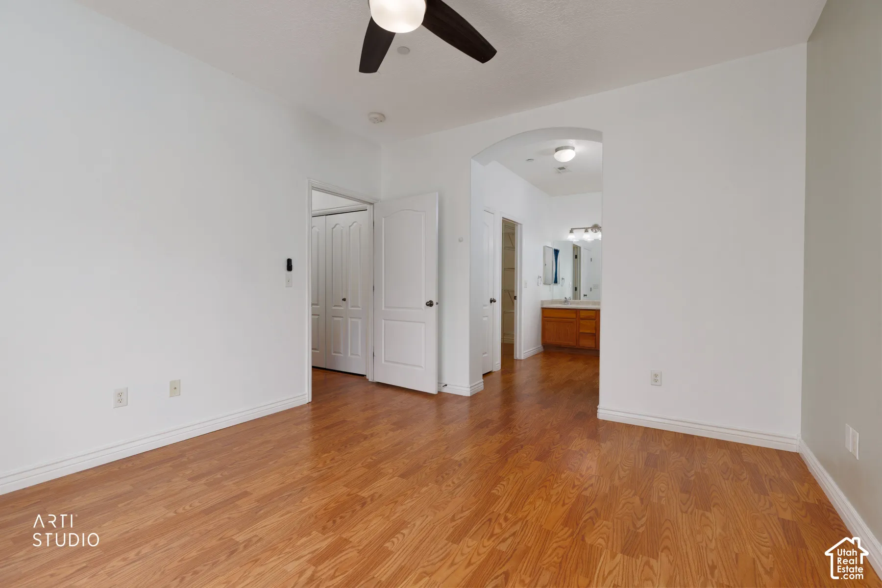 Spacious room featuring wood-finish flooring, a ceiling fan, and access to a bathroom with a double vanity