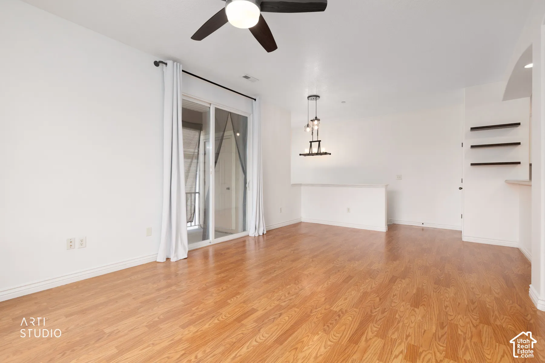 Spacious living area featuring wood-finish flooring, a ceiling fan, and a sliding glass door with balcony access