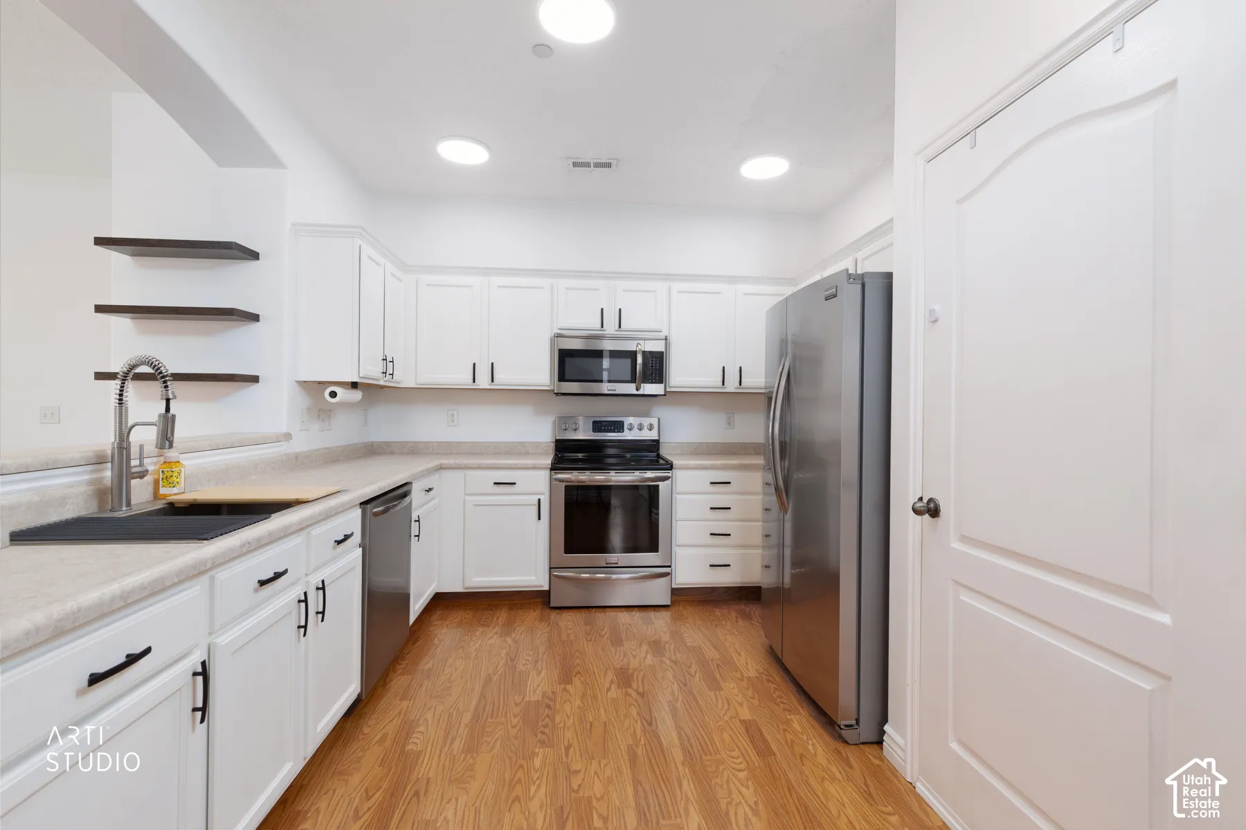Kitchen featuring white cabinetry, stainless steel appliances, wood-finish flooring, light-toned countertops, and open shelving