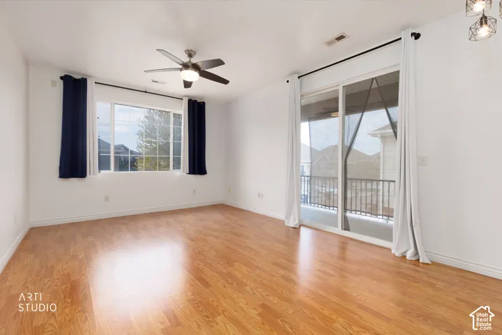 Spacious room featuring wood-finish flooring, a ceiling fan with integrated lighting, and a large window with white trim