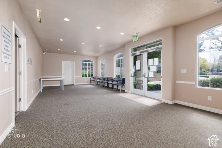 Spacious room featuring neutral carpeting, recessed lighting, arched windows with grid patterns, a glass-paneled entry door, and painted trim molding