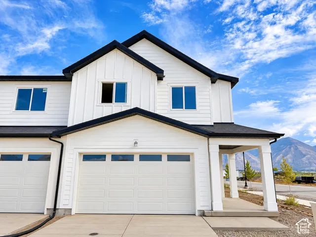 Modern farmhouse exterior featuring white siding, black trim, a covered porch with square columns, and two garage doors with upper window panels