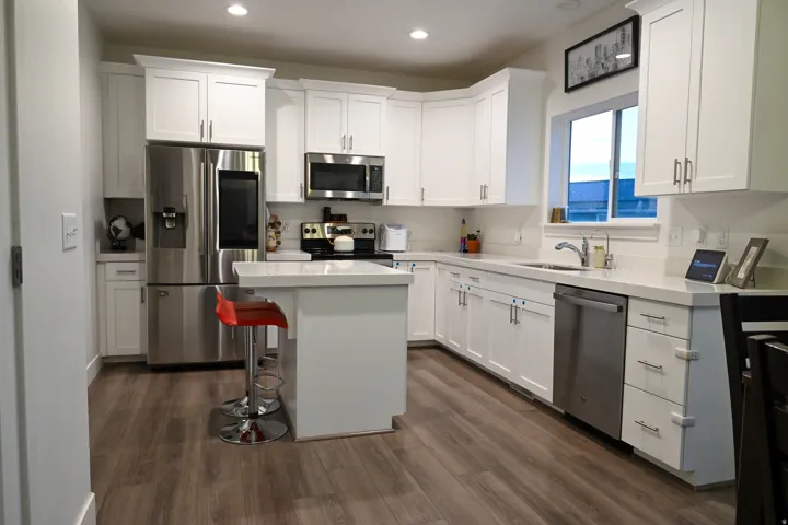Modern kitchen featuring white shaker cabinetry, stainless steel appliances, a center island with counter seating, light-toned countertops, and wood-finish flooring